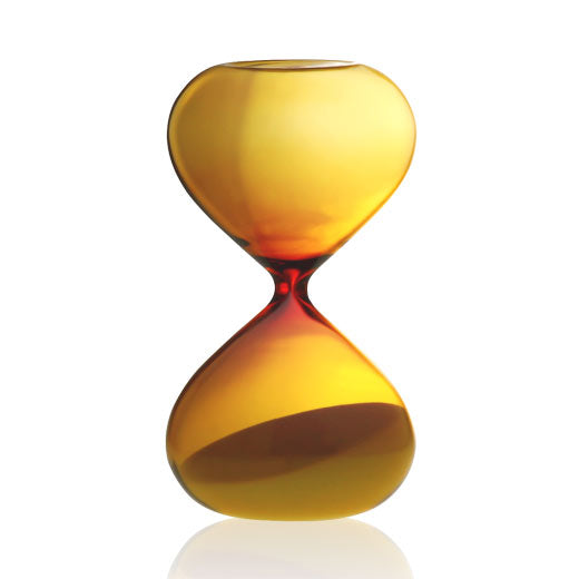 Amber glass hourglass with rounded bulbs, sand collected in the lower chamber, on a white background.