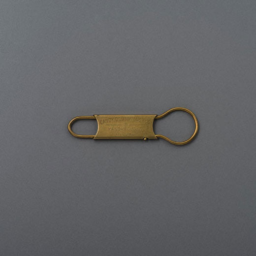 Brass GORDON key ring with engraved flat plate and looped wire ends, on a grey background.