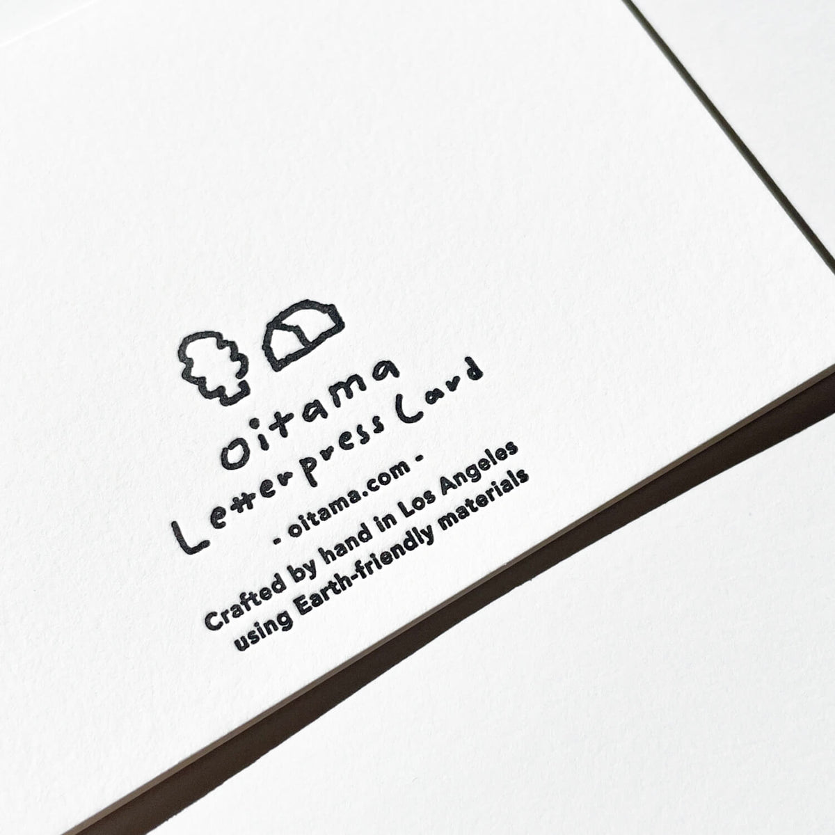 Close-up of the back of a white letterpress card showing the Oitama logo and hand-crafted text.