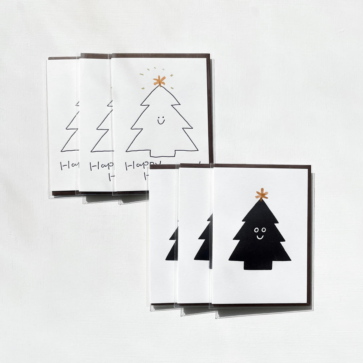 Two overlapping groups of letterpress cards showing smiling Christmas trees, one outlined and one solid black, each topped