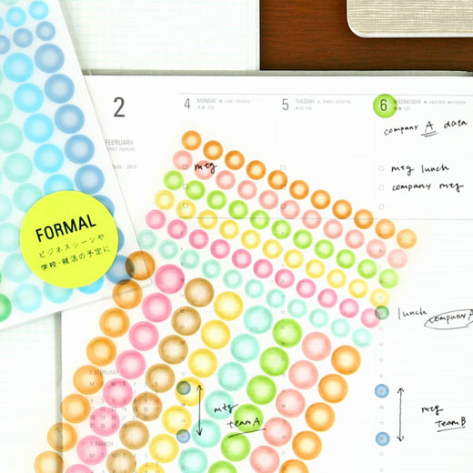Sheets of colorful see-through dot stickers laid over an open planner with handwritten notes and dates marked.